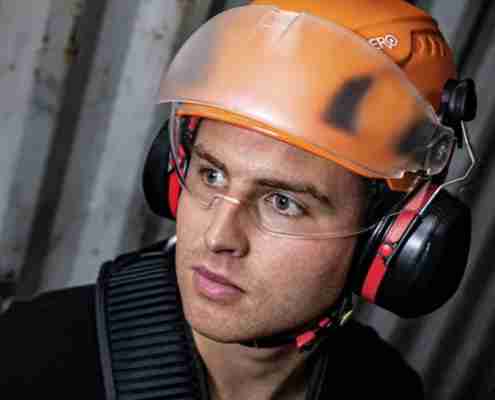 Close up portrait of a site worker wearing a Zero Apex safety helmet with integrated hearing protection ear muffs and a clear half face visor.